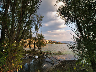 View through the trees of Lake Orestiada  and Kastoria city at sunset time,  beautiful light, reflections on lake water.