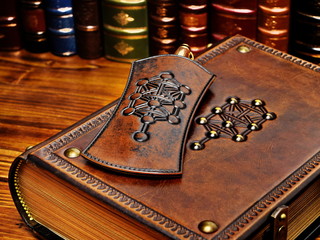 Thick leather book and pen holder lay down to the table with books in the background. The tree of life symbol are on both items. - obrazy, fototapety, plakaty