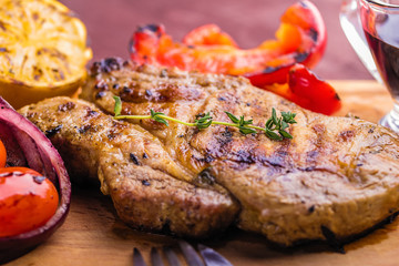 Juicy pork steak with a sprig of fresh thyme, lemon and grilled vegetables close-up