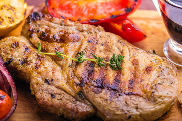 Juicy pork steak with a sprig of fresh thyme, lemon and grilled vegetables close-up