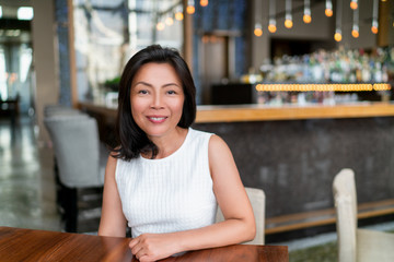 Asian middle age business woman smiling portrait. Happy elegant mature Chinese businesswoman lady in fancy restaurant setting.