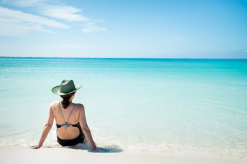 Fototapeta na wymiar Woman with a sun hat sitting on the beach. La Tortuga Island, Venezuela