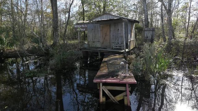Front tracking shot of a small wooden cottage with a dingy and abandoned boat in the swamps of New Orleans, Louisiana.