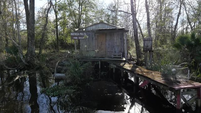 Dolly shot of a small wooden cottage with a dingy and abandoned boat in the swamps of New Orleans, Louisiana.