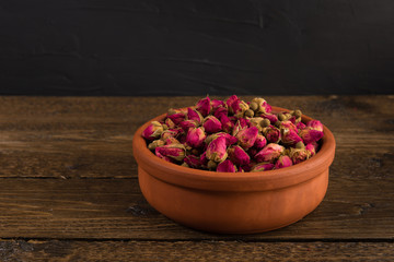 tea rose buds in a clay pot isolated on wooden table on black background