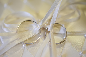 Dos anillos de boda enlazados con lazo blanco de seda