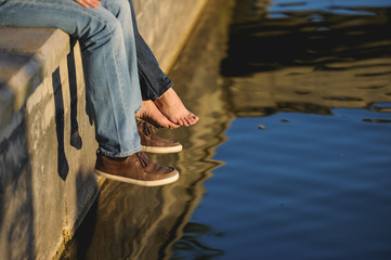 piernas y pies de hombre y mujer sentados en el muelle de un puerto