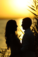 Silueta de pareja en atardecer con lago y hojas al fondo