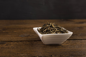 dry green tea in a white bowl isolated on wooden table on black background