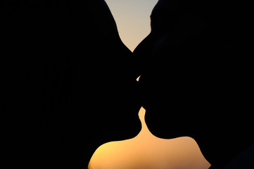 Silueta en pimer plano de caras de hombre y mujer besándose con el atardecer en el fondo