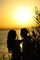 Silueta de pareja en atardecer con lago y hojas al fondo