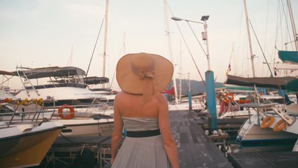 Lady in dress walking on holiday in luxury yacht and sailboats marina pier.