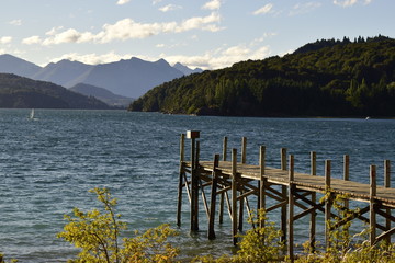 se ve un muelle en un lago rodeado de montañas boscosas
