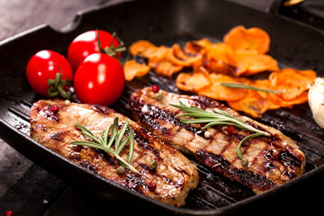 Grilled beef steak with vegetables and spices on black background