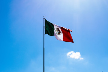 Mexican Flag against clear blue sky and sun 