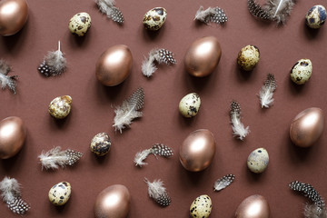 Easter background. Easter egg pattern of bronze painted eggs, quail eggs and feathers on brown background.