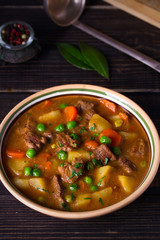 Homemade Irish beef stew with potatoes, carrots and peas in bowl on wooden table. vertical