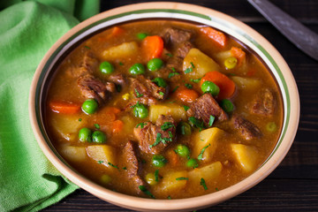 Homemade Irish beef stew with potatoes, carrots and peas in bowl on wooden table.  horizontal