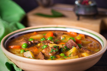 Homemade Irish beef stew with potatoes, carrots and peas in bowl on wooden table.  horizontal
