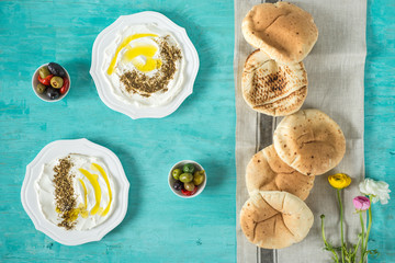 labneh labaneh)middle eastern soft goat's milk cheese with olive oil, za'atar, lemon,pita bread ,served at traditional concept over rustic turquoise wooden plate, flowers, flatlay,top view,copy space