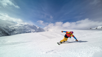 Active man snowboarder riding on slope during beautiful sunny day in the ountains.