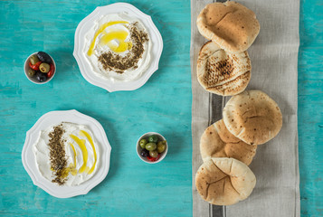 labneh labaneh)middle eastern soft goat's milk cheese with olive oil, za'atar, lemon,pita bread ,served at traditional concept over rustic turquoise wooden plate, flowers, flatlay,top view,copy space