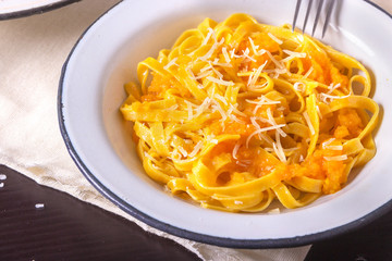 Pumpkin tagliatelle pasta with pumpkin cream parmesan cheese in white plate on dark background