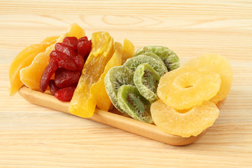 Dried pieces of kiwi, papaya, mango, pineapple and strawberry fruits, lying on a bamboo plate on a wooden table. Macro. Closeup