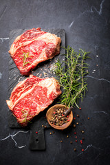 Raw Fresh Marbled Meat Beef Steak rosemary, spices slate on board. Black marble background. Top View Copy space for Text