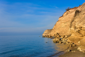 Fototapeta na wymiar High gravel cliff by blue Greek sea on sunny day