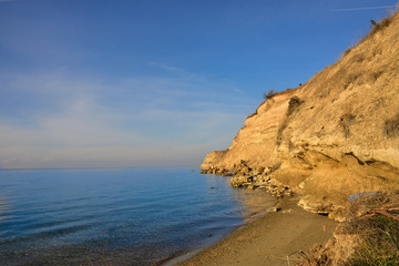 High gravel cliff by blue Greek sea on sunny day