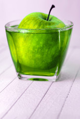  green apple in a glass of juice on a wooden background.
