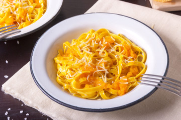 Pumpkin tagliatelle pasta with pumpkin cream parmesan cheese in white plate on dark background