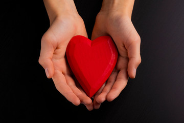 Hands of a teenager child holding a red wooden heart in their hands.