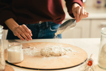 Obraz na płótnie Canvas Woman holding flour scoop and sifting flour on the dough