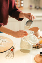 Woman holding glass jar and taking flour from it