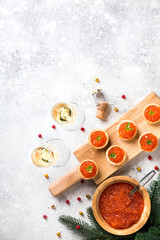 Christmas and New Year holidays composition. Red Salmon Caviar in wooden bowl, Tartlets Festive Appetizer and champagne on  gray background.Copy space for Text.