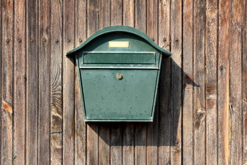 Dark green metal vintage retro mailbox with lock mounted on wooden boards barn wall on warm sunny day