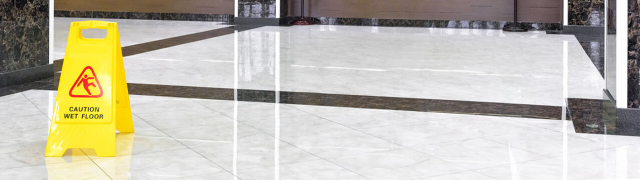 Marble shiny floor in luxury hallway of company or hotel during cleaning. Panorama of washed cleaned floor with sign of caution wet floor. Professional care service of the office interior.