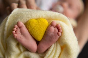 baby feet on yellow background. feet of a newborn baby. little foot. toy heart in legs