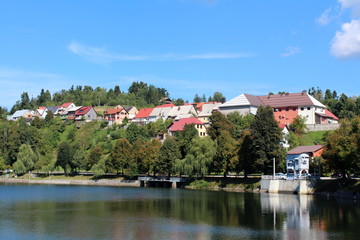 Fototapeta na wymiar Densely built traditional mountain houses of small mountain town next to fresh water lake surrounded with trees and other forest vegetation on warm sunny day