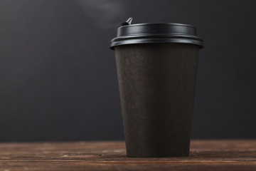 Black background, hot take-away coffee on a wooden table. Cafe menu design concept