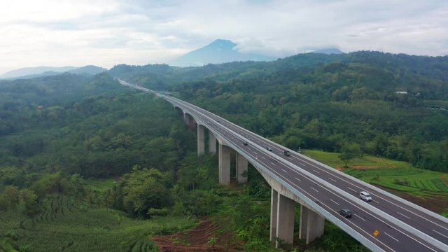 Aerial view of Trans-Java Toll Way bridge with green forest view and fast traffic on misty morning in Bawen, Central Java, Indonesia. Shot in 4k resolution