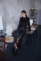 Beautiful brunette woman wear casual fashion style clothes pretty face total black pullover long lather skirt accessory shoes in interior art, workshop, artist sculpture sculptor makeup.