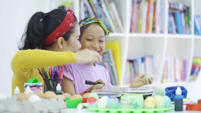 Cheerful girl and her mother coloring easter eggs on the table at home. Shot in 4k resolution