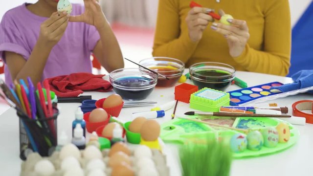 Cute little girl and her mother coloring easter eggs with dyes and colorful marker on the table at home. Shot in 4k resolution