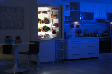 Stylish kitchen interior with refrigerator full of products at night