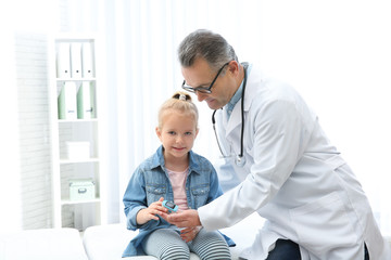 Doctor checking little girl's pulse with medical device in hospital