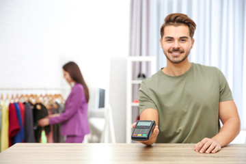 Male shop assistant with payment terminal at counter. Space for text
