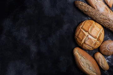 Rolgordijnen Vers brood op een zwart bord. Bovenaanzicht met kopieerruimte © zakiroff